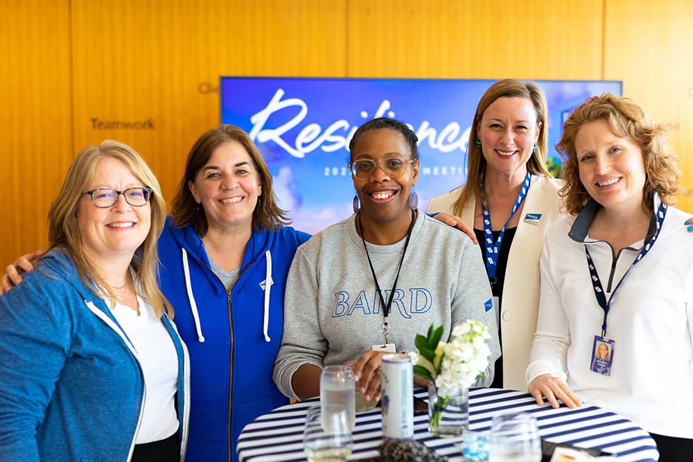 Group of five women standing together at a reception table wearing Liberty branded clothing.