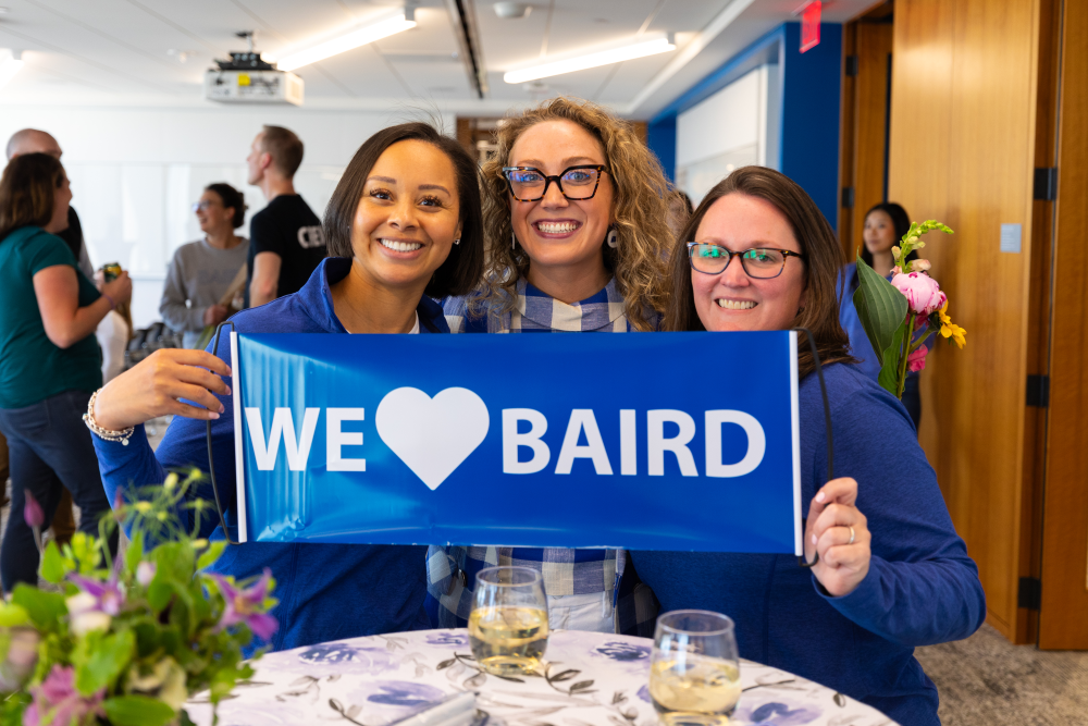 Three women holding a We Love Liberty sign while attending the Liberty Annual Meeting