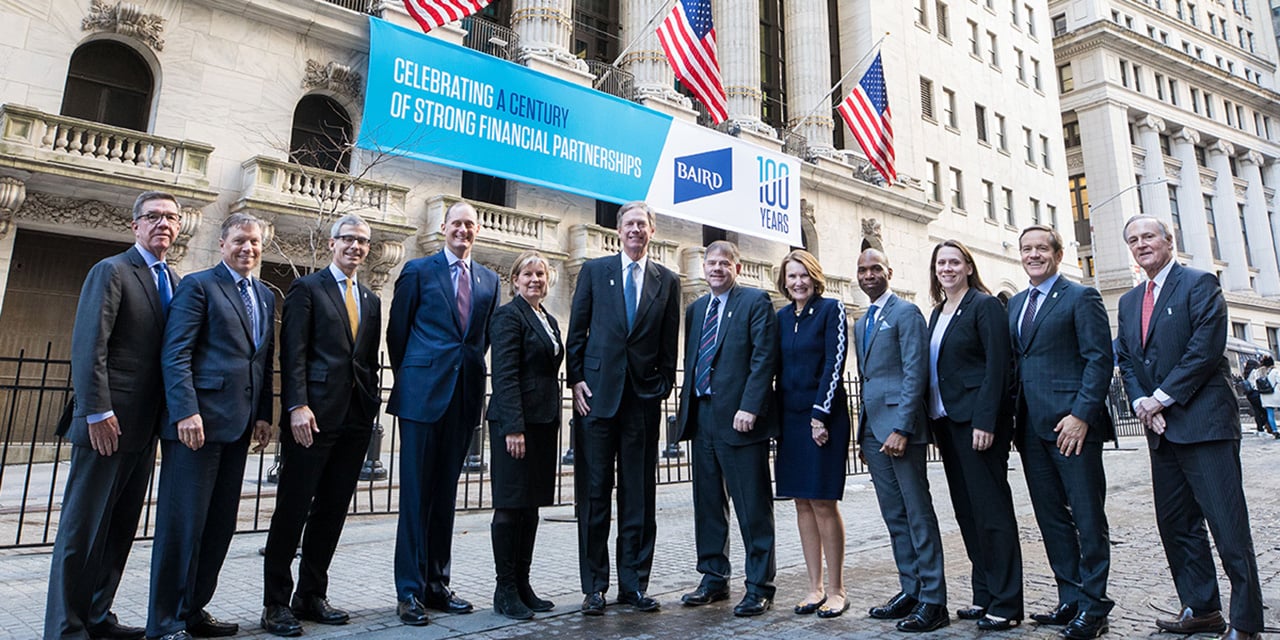  Liberty leadership standing in front of the New York Stock Exchange with a banner celebrating Liberty 's 100th anniversary in the background.